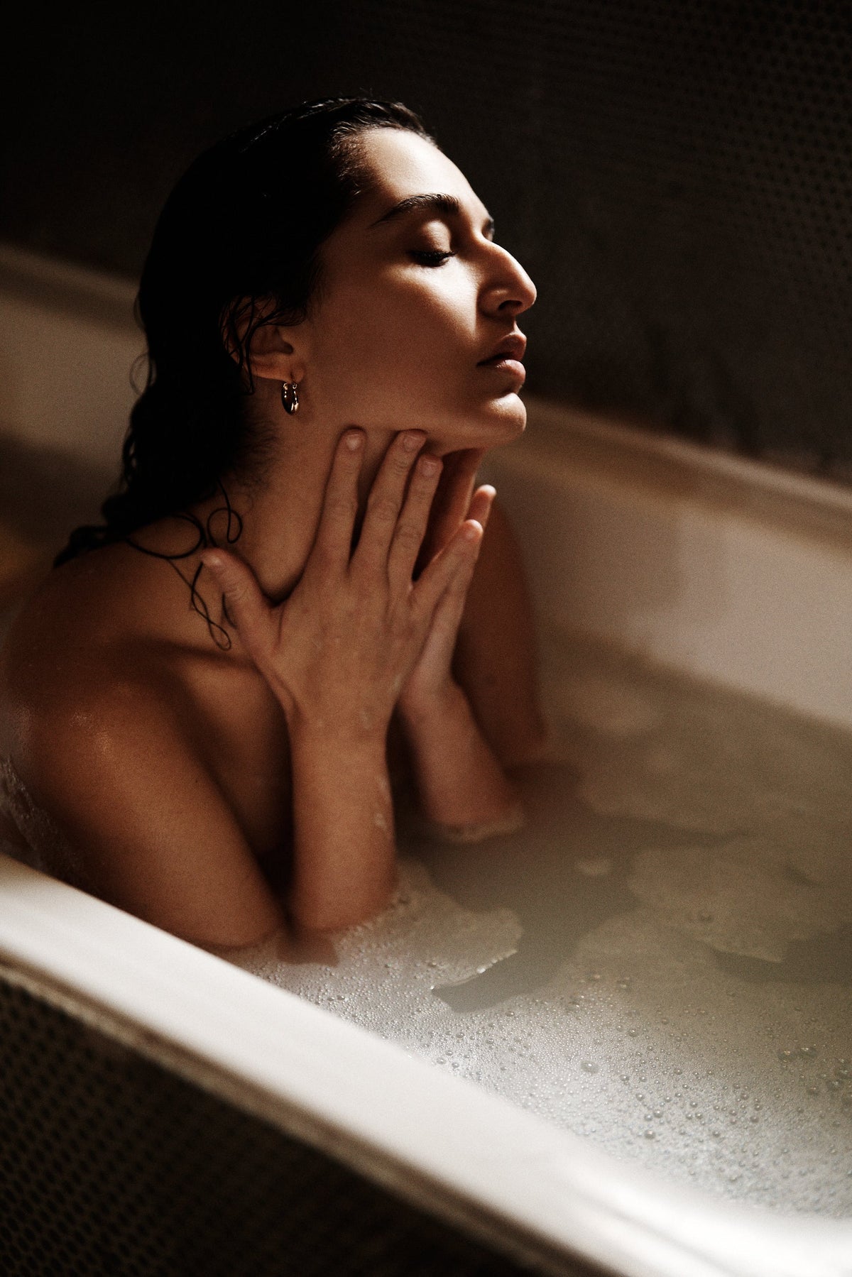 Woman taking a bath with mood lighting and her hands on her neck
